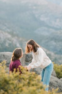 Lesbian couple celebrating after their engagement with one girl still on her knee at glacier point in yosemite with the valley view below