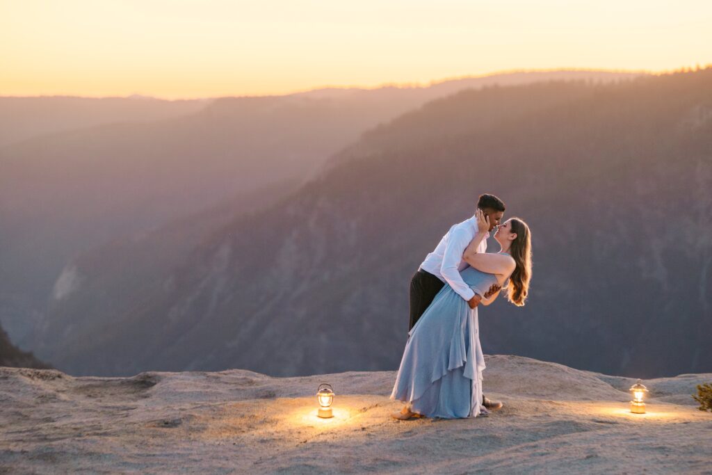 Couple dancing during golden hour at Taft Point in Yosemite with camping lanterns glowing while he dips her for a kiss