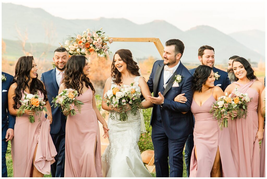 Wedding party walking and laughing in pink dresses and navy suits