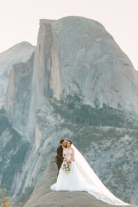 Groom and Bride standing on a rock with half dome towering behind them