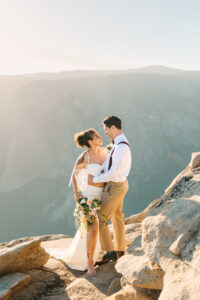 bride and groom holding each other and grinning while at taft point in Yosemite