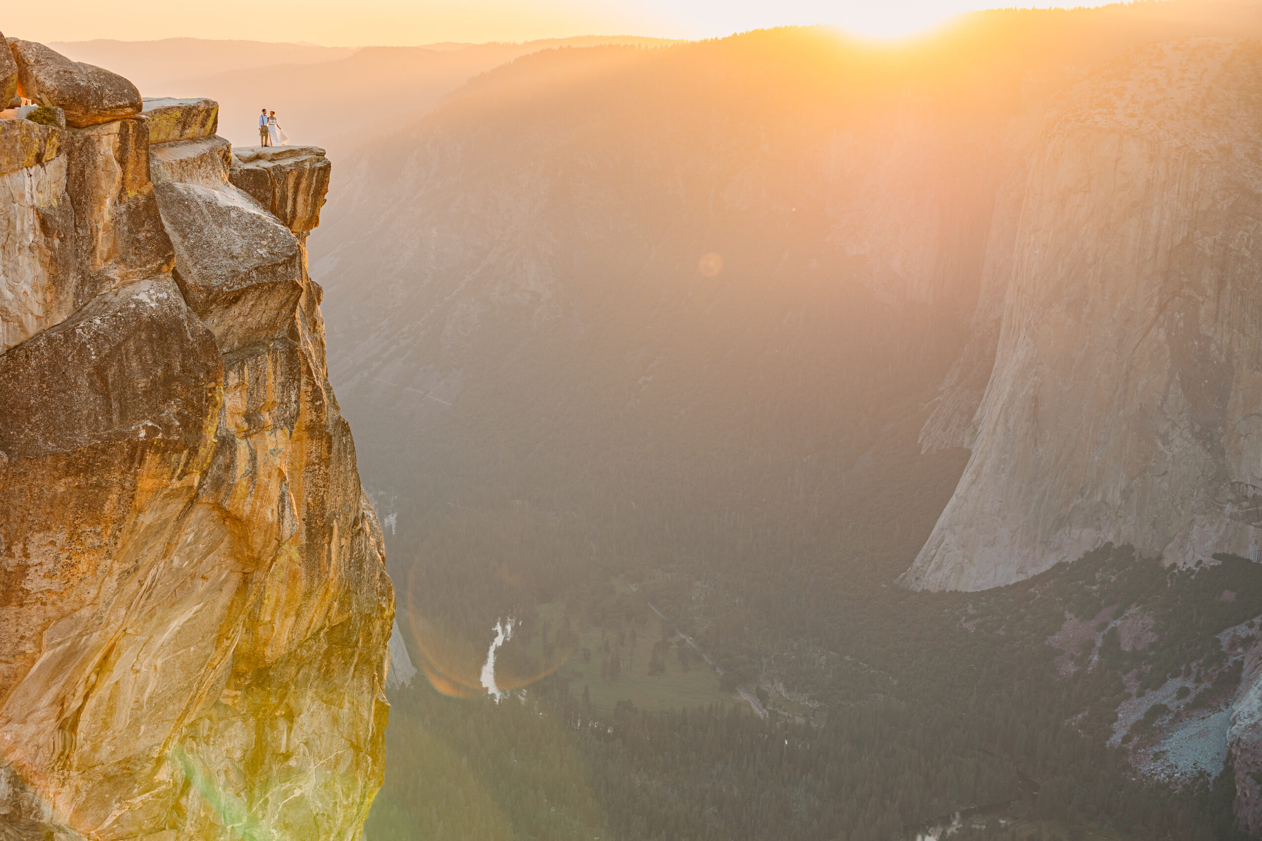 Dramatic cliffside sunset image with pink and orange skies at Taft Point in Yosemite. Bride and Groom dancing on the cliff overlooking the Yosemite Valley.
