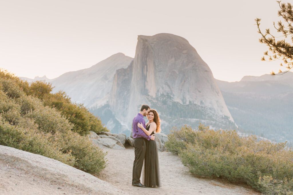 couple snuggling at glacier point with half dome towering in the background during sunrise