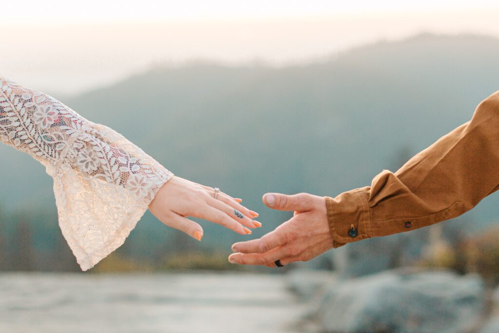 Couple reaching to hold hands with the mountains in the background