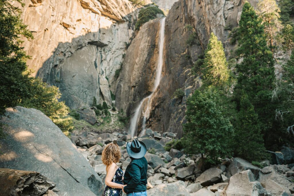 Couple looking upon Lower Yosemite Falls from the base of the fall while the waterfall flows