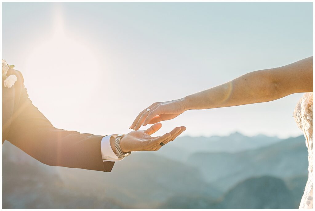 Bride and groom reaching for each other’s hands during their intimate elopement with a scenic mountain backdrop.