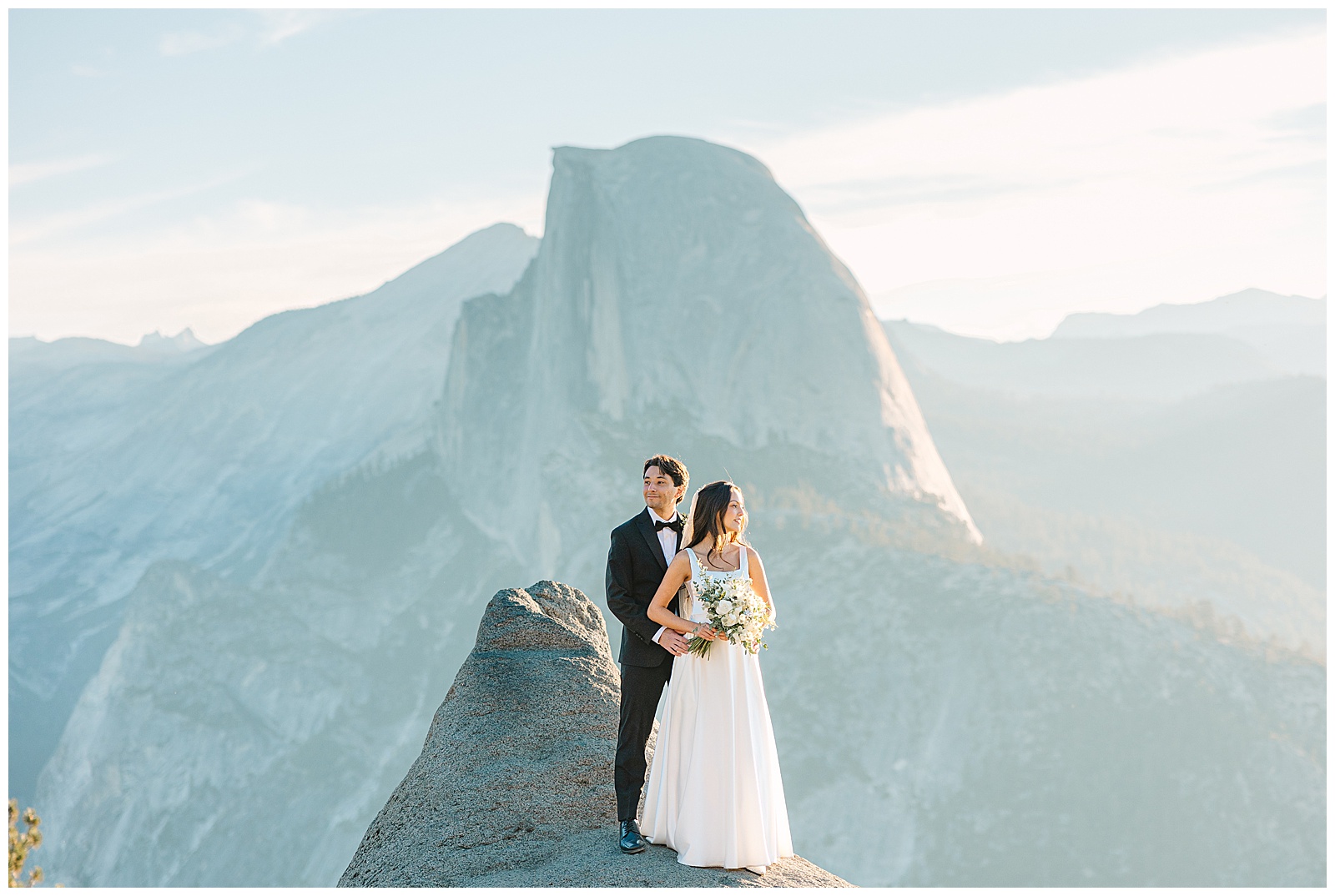 Bride and groom standing together on a rock ledge with Half Dome in the background at Yosemite National Park