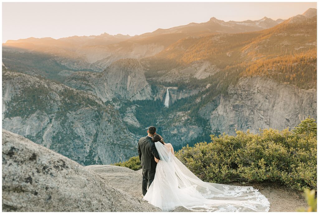 bride and groom hugging from the side while they watch the sunrise over the yosemite valley from glacier point. Bride rests her head on the grooms shoulder